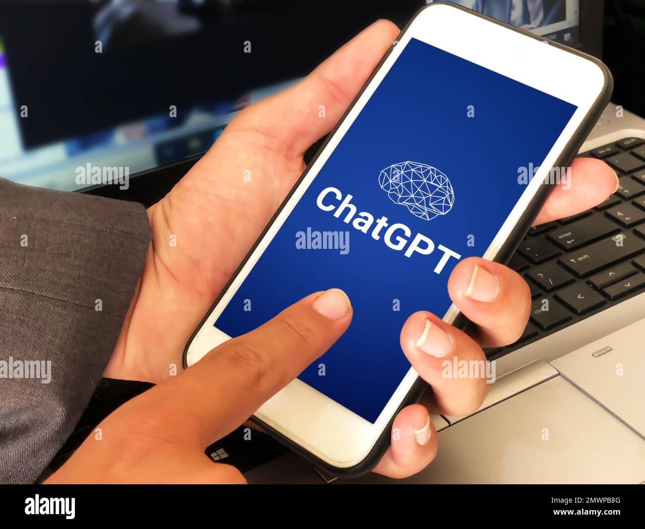 28.1. United Satates. Man using ChatGPT on Mobile with blue background and laptop in the backdrop. Modern ai writing tool using concept editorial wall Stock Photo