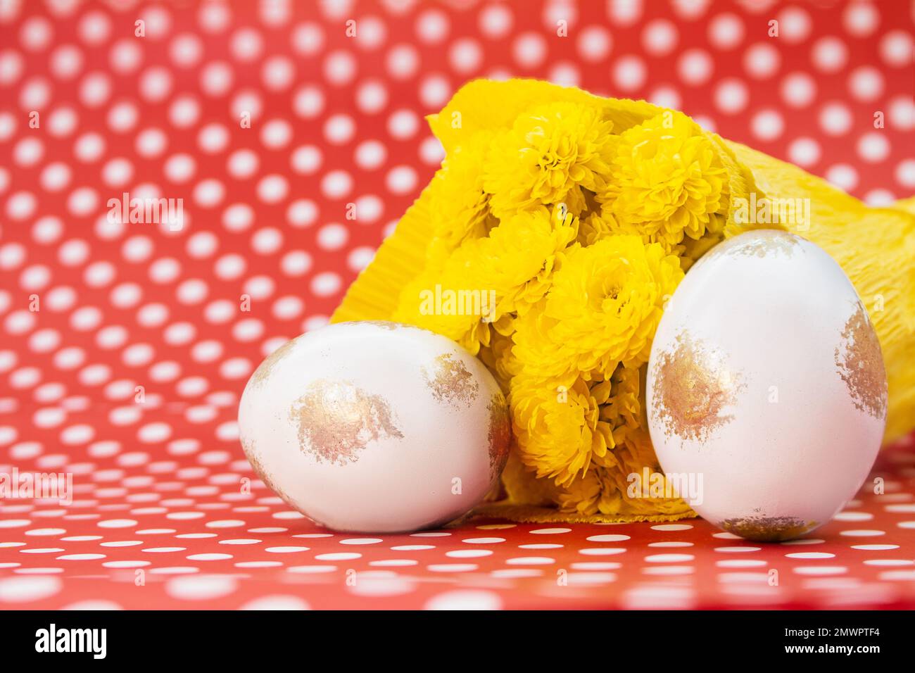 White gold eggs with bouquet of yellow chrysanthemums on red with polka dots background. Easter. Copy space Stock Photo