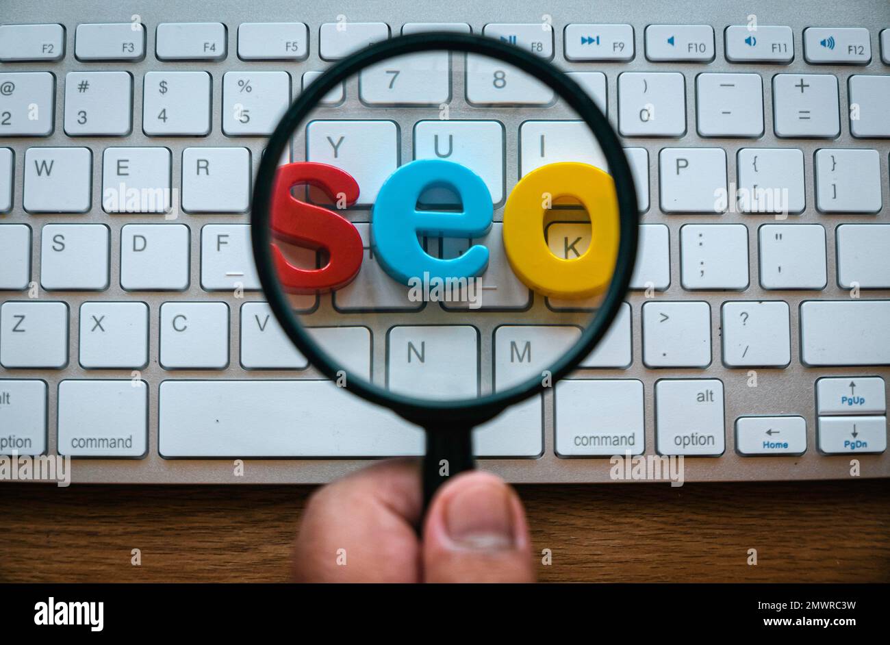 Search engine optimization concept. A hand holding magnifying glass magnify a word seo on a computer keyboard. Stock Photo