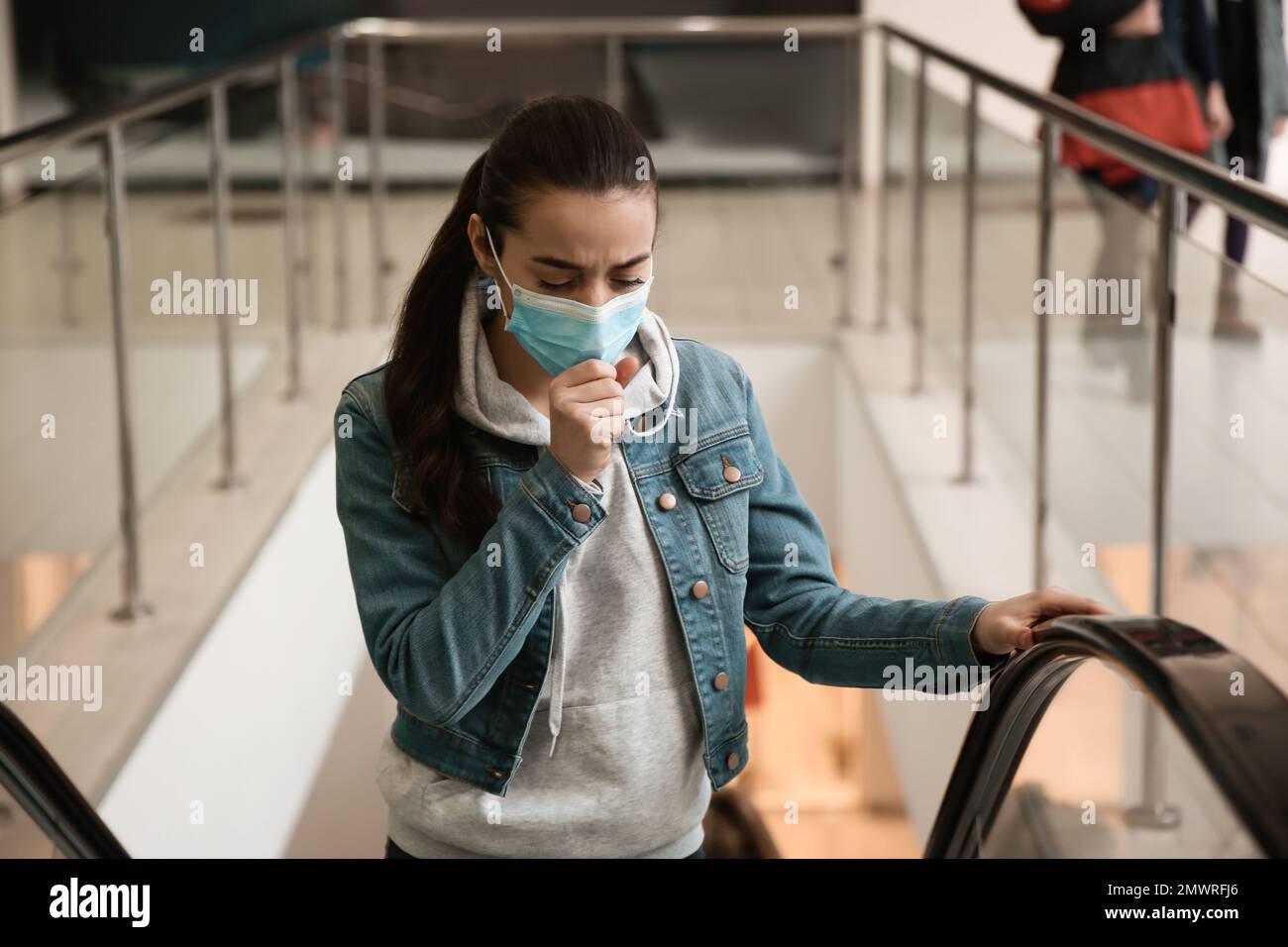 Young woman with disposable mask on escalator in mall. Dangerous virus ...