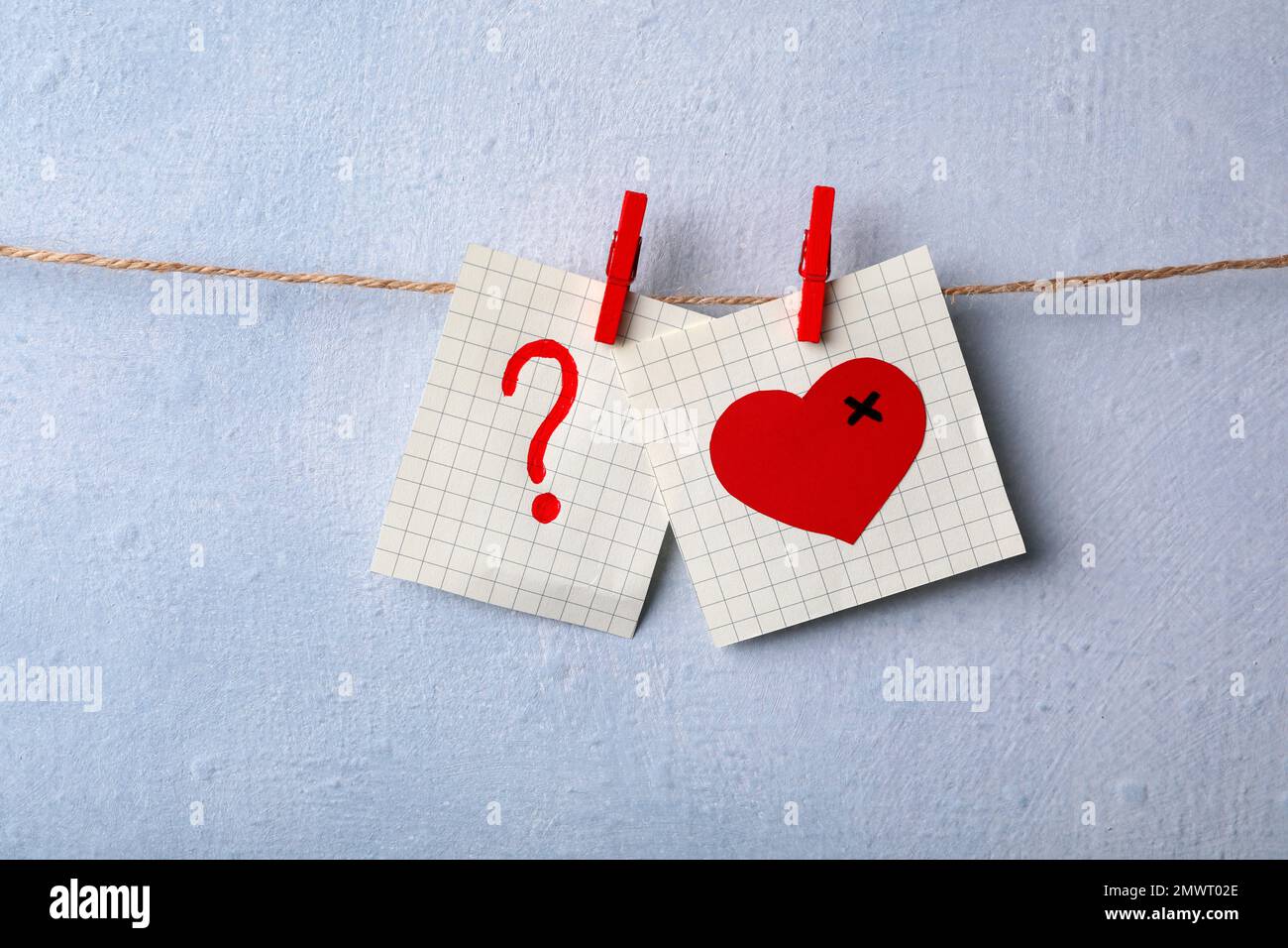 Paper notes with drawings of heart and question mark pinned on laundry string near light wall. Relationship problems concept Stock Photo