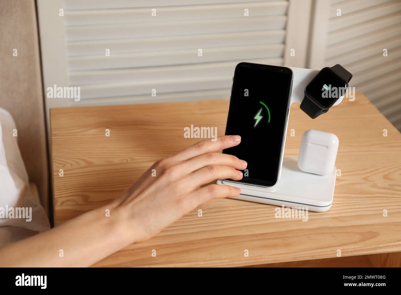 Woman taking smartphone from wireless charger in bedroom, closeup Stock Photo
