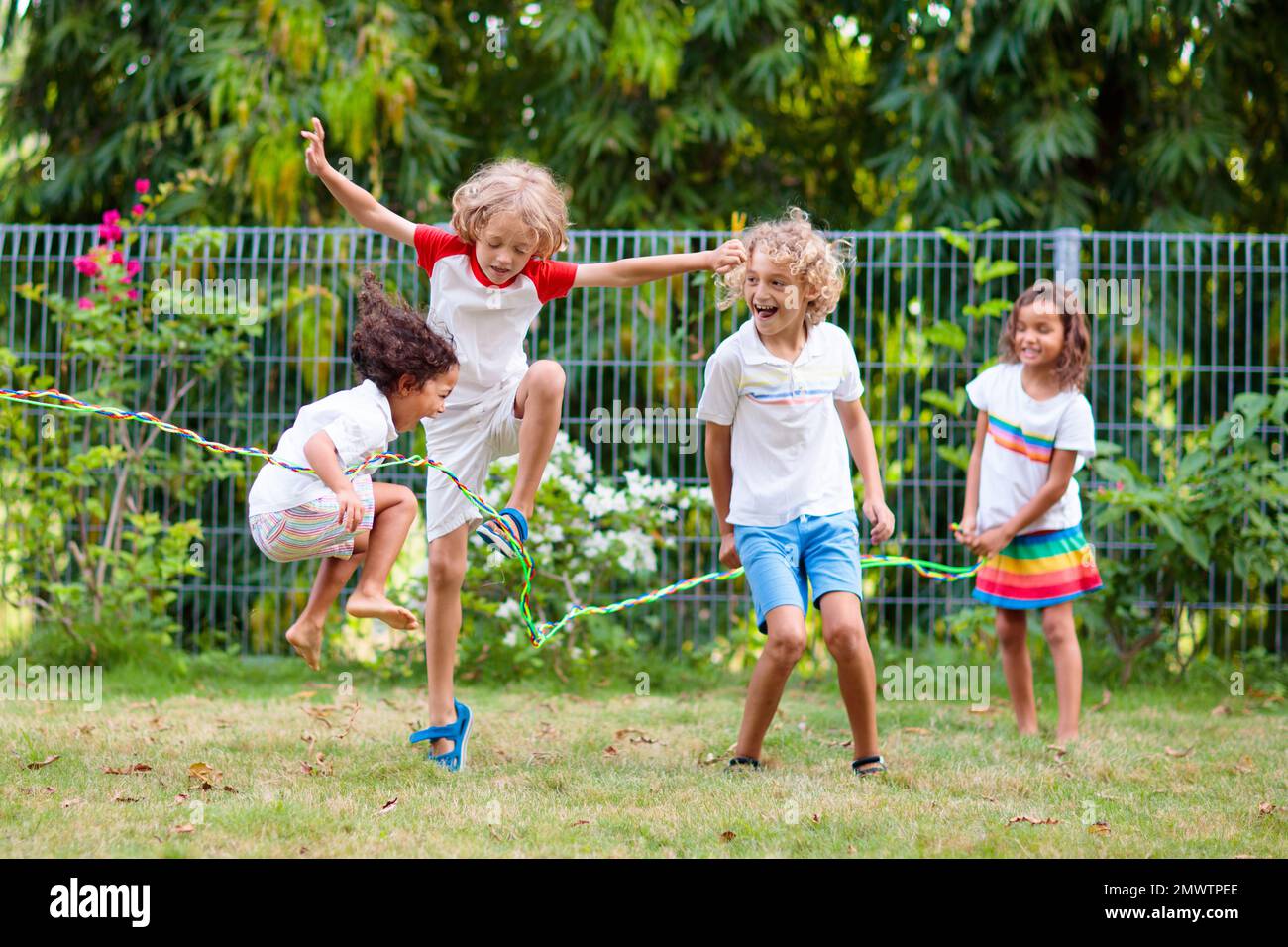 Happy kids play outdoor. Children skipping rope in sunny garden. Summer