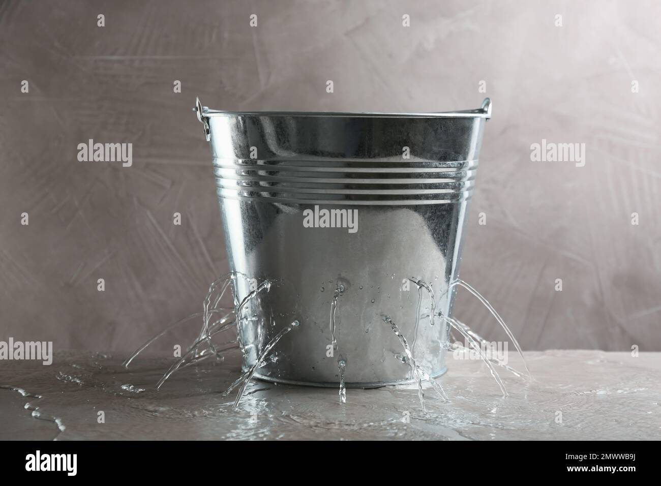 Leaky bucket with water on table against grey background Stock Photo