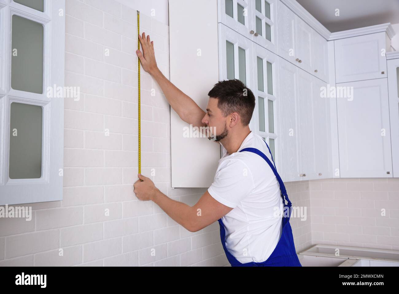 Worker using measuring tape while installing new furniture in kitchen Stock Photo