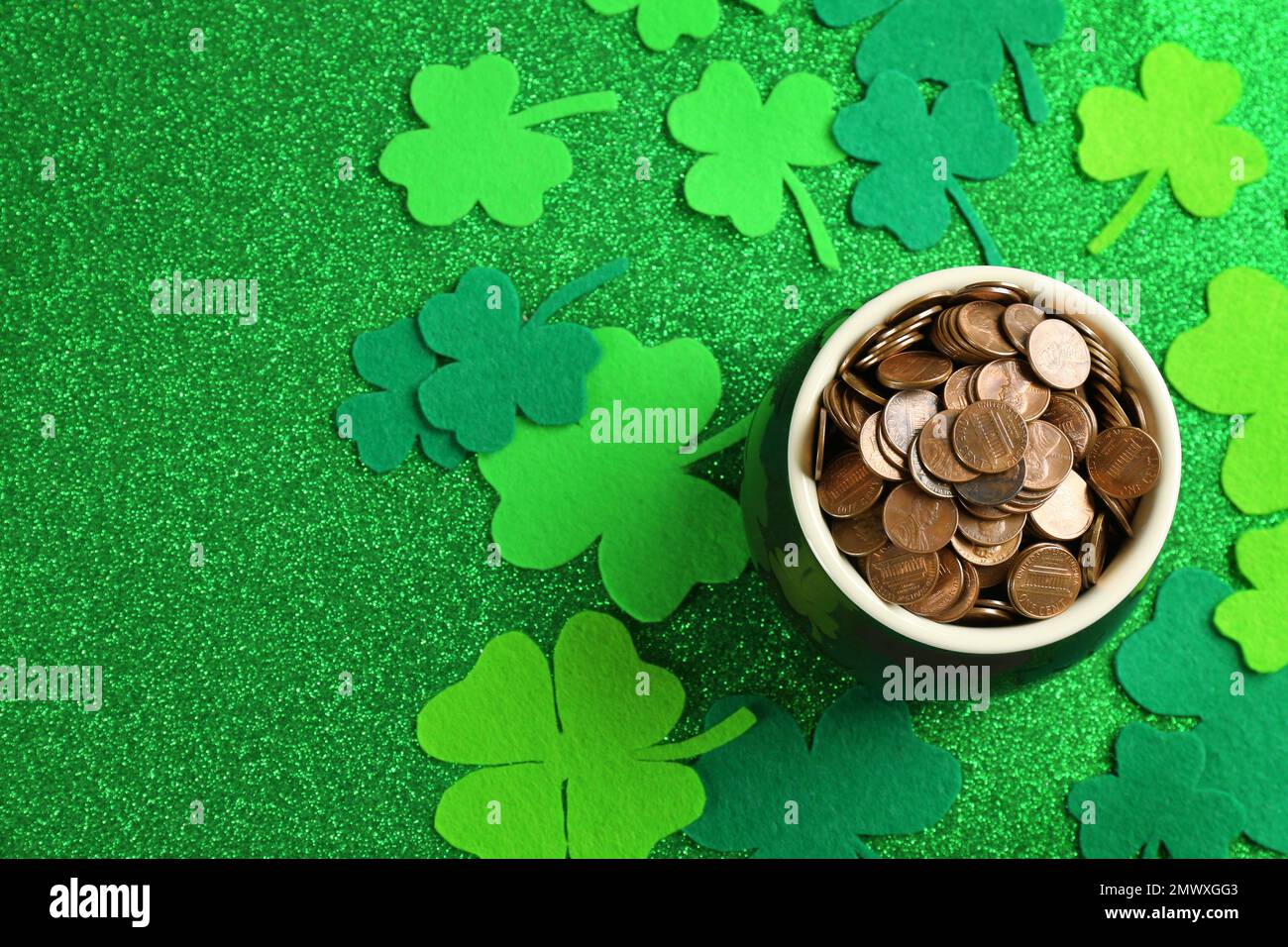 Pot of gold coins and clover leaves on green background, flat lay. St ...