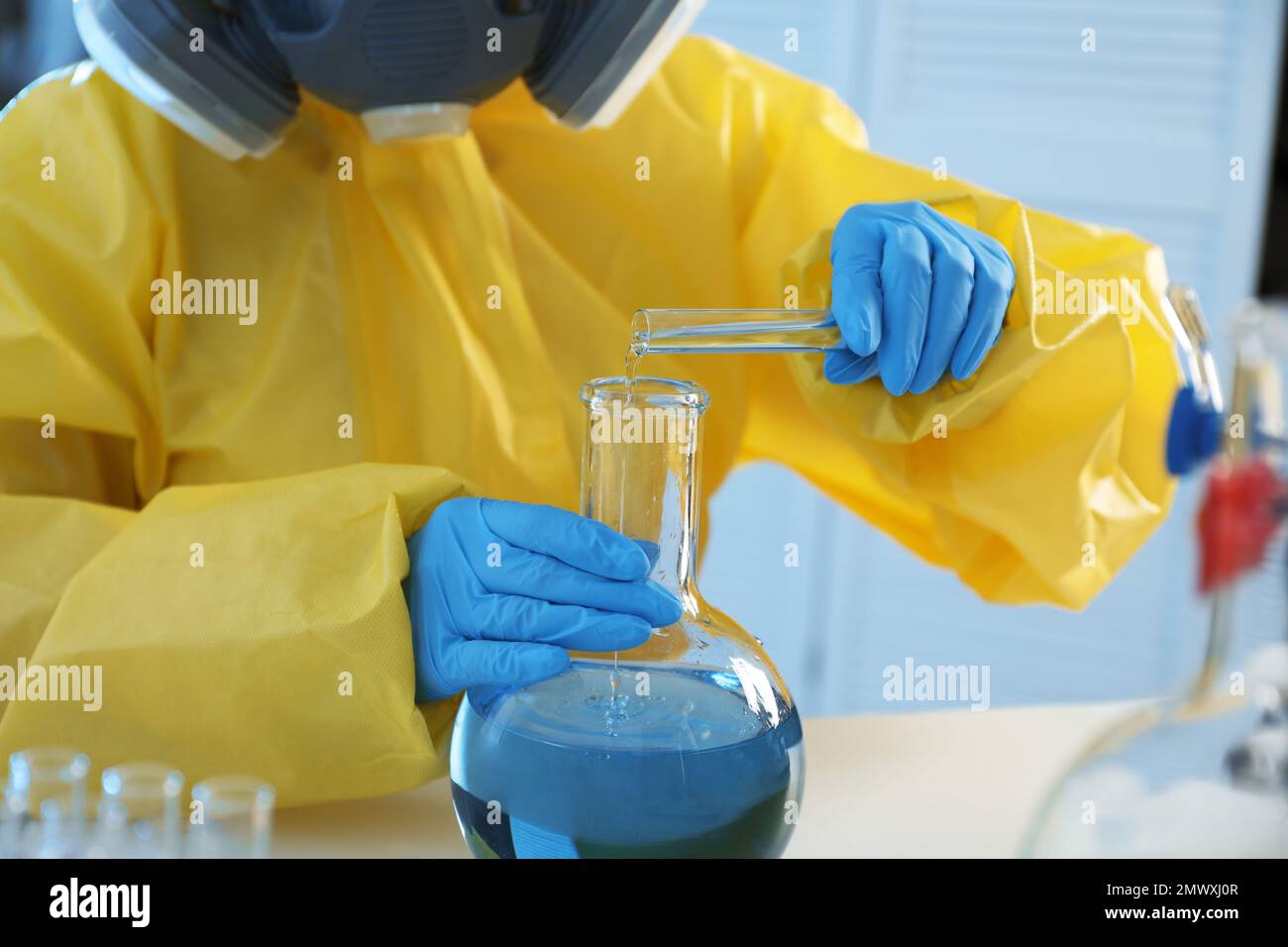Scientist in chemical protective suit pouring reagent into flask at