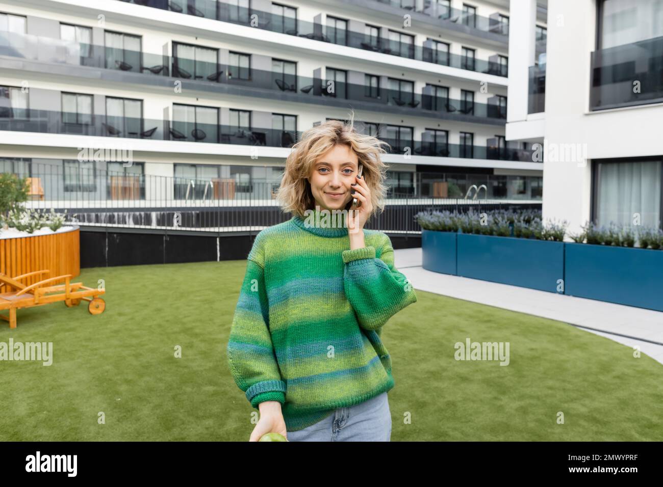 cheerful young woman in green sweater talking on smartphone near hotel building in Barcelona,stock image Stock Photo