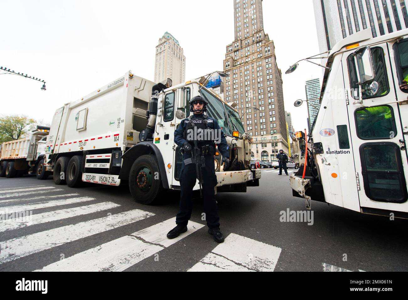 An NYPD police officer stands guard in front of garbage trucks on 59th