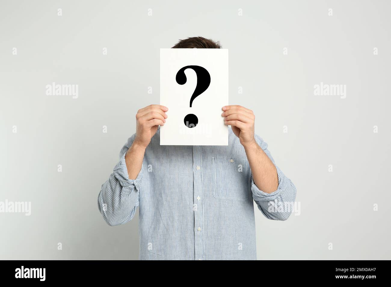 Man holding question mark sign on light background Stock Photo - Alamy