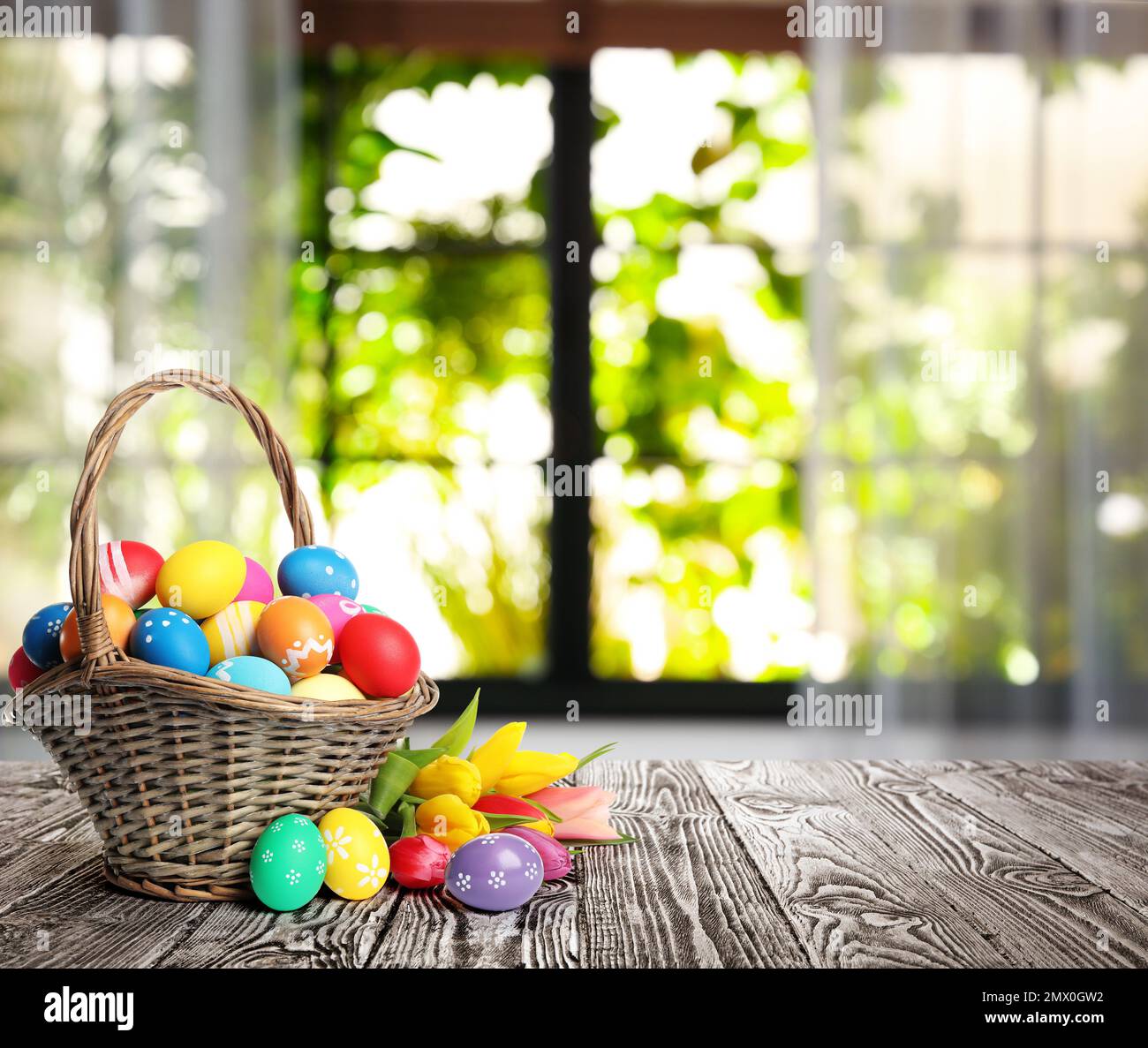 Bright Easter eggs in wicker basket on table indoors. Space for text Stock Photo