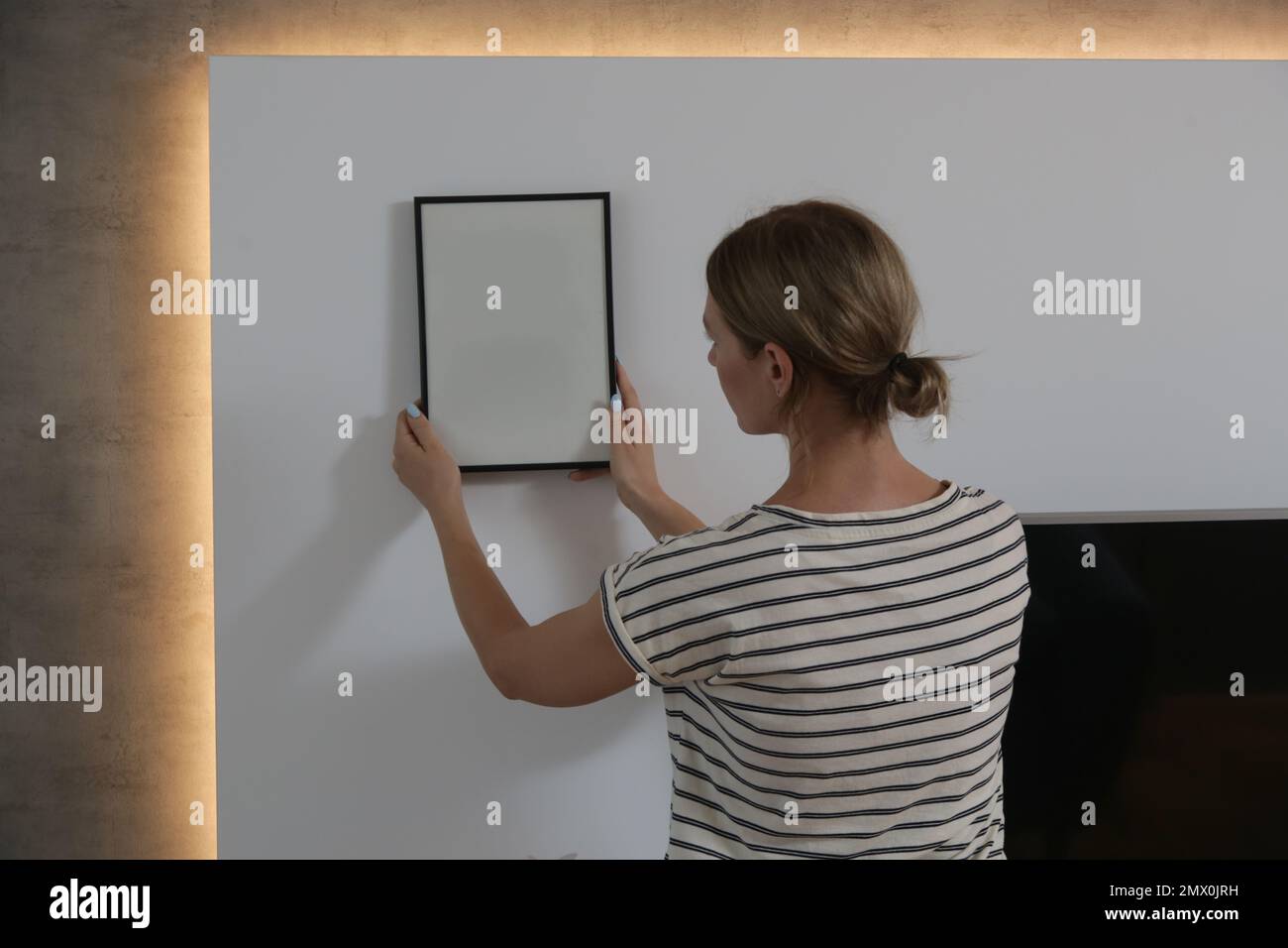 Woman arranging picture frames on wall in new house, diy home improvement concept Stock Photo