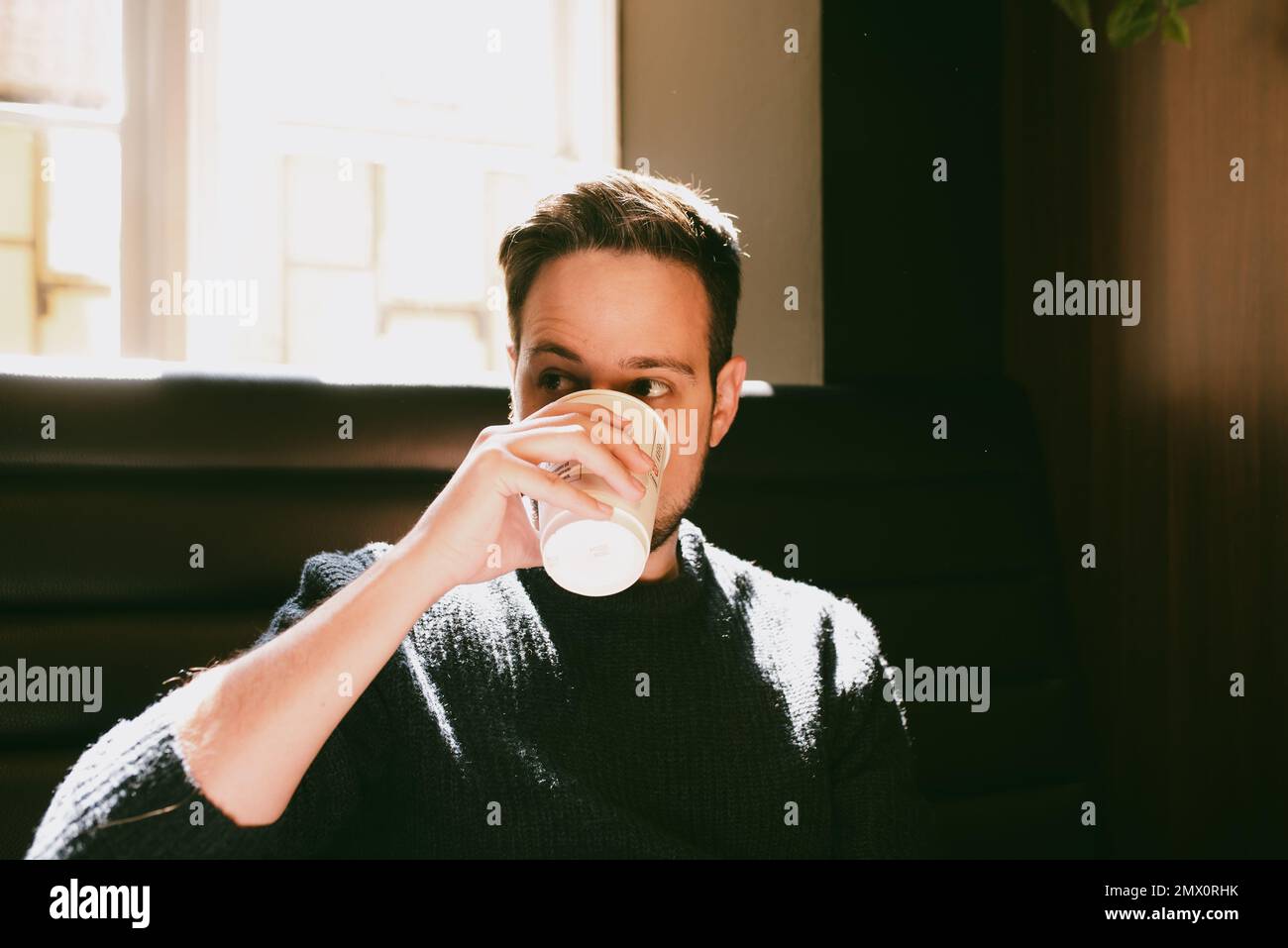 Man drinking coffee in a paper cup inside a coffee shop Stock Photo