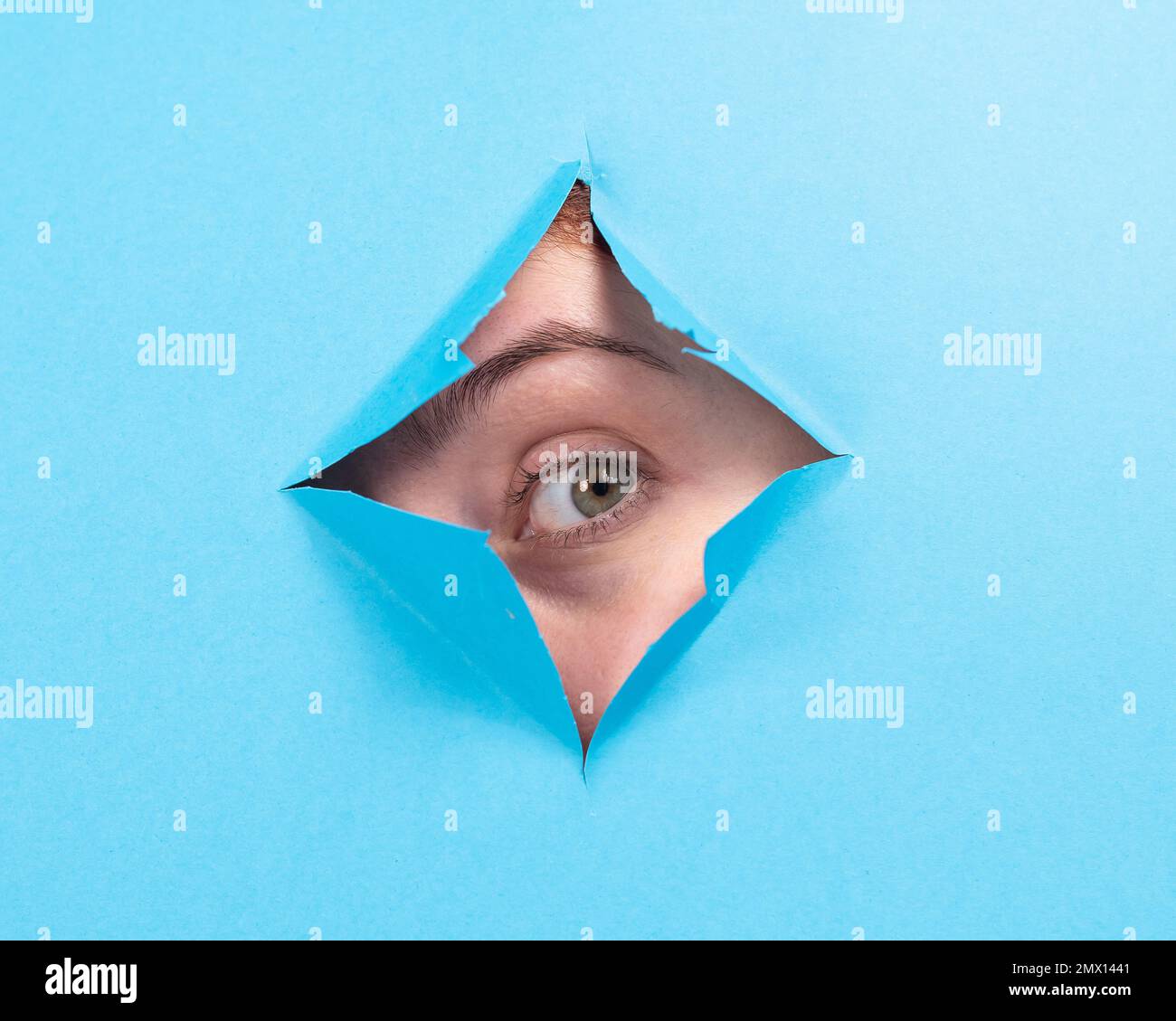 Woman peeking out of hole in blue paper background.  Stock Photo
