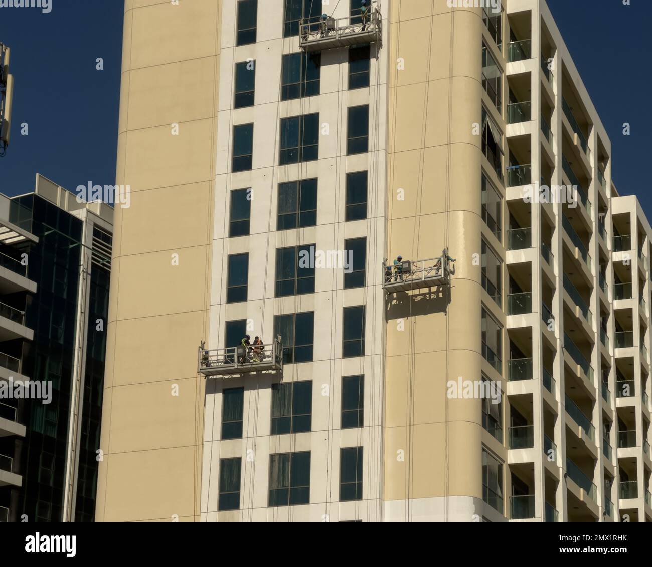 Dubai, United Arab Emirates - 7th January, 2022: Construction workers painting the exterior facade of a residential building, lowered on suspended sca Stock Photo