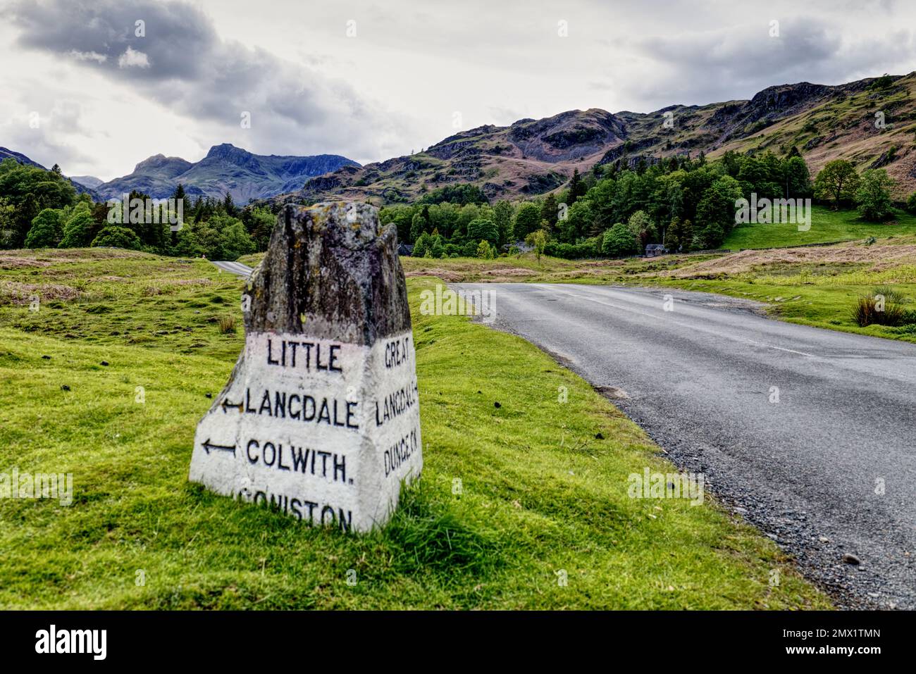 Lake District, Cumbria, England, UK - Old fashioned milestone on road outside Elterwater village with mountain peaks of the Langdale Pikes in distance Stock Photo