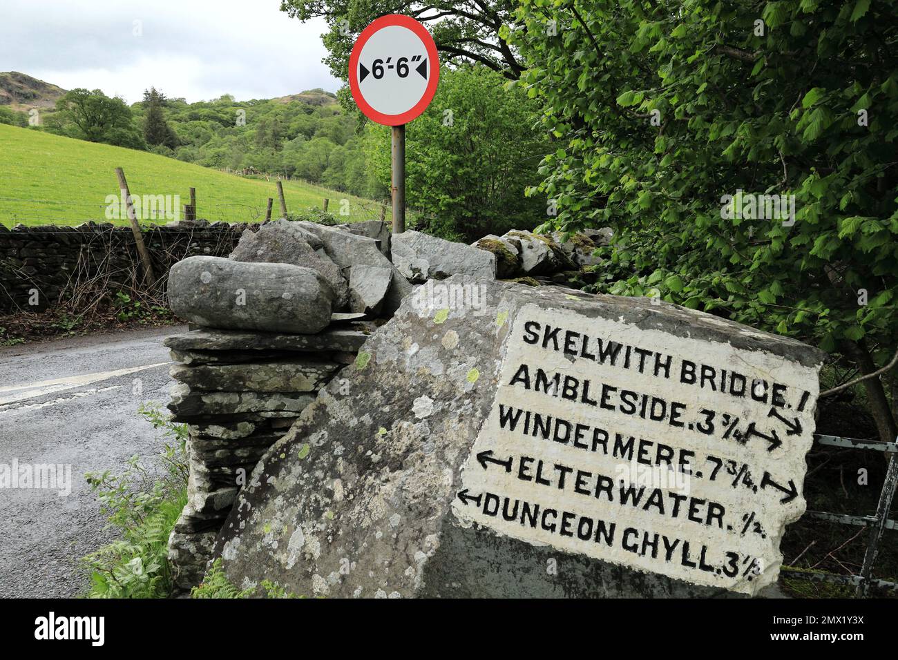 Country lane with milestone and vehicle width restriction sign in Elterwater, Lake District, England, Cumbria, UK Stock Photo