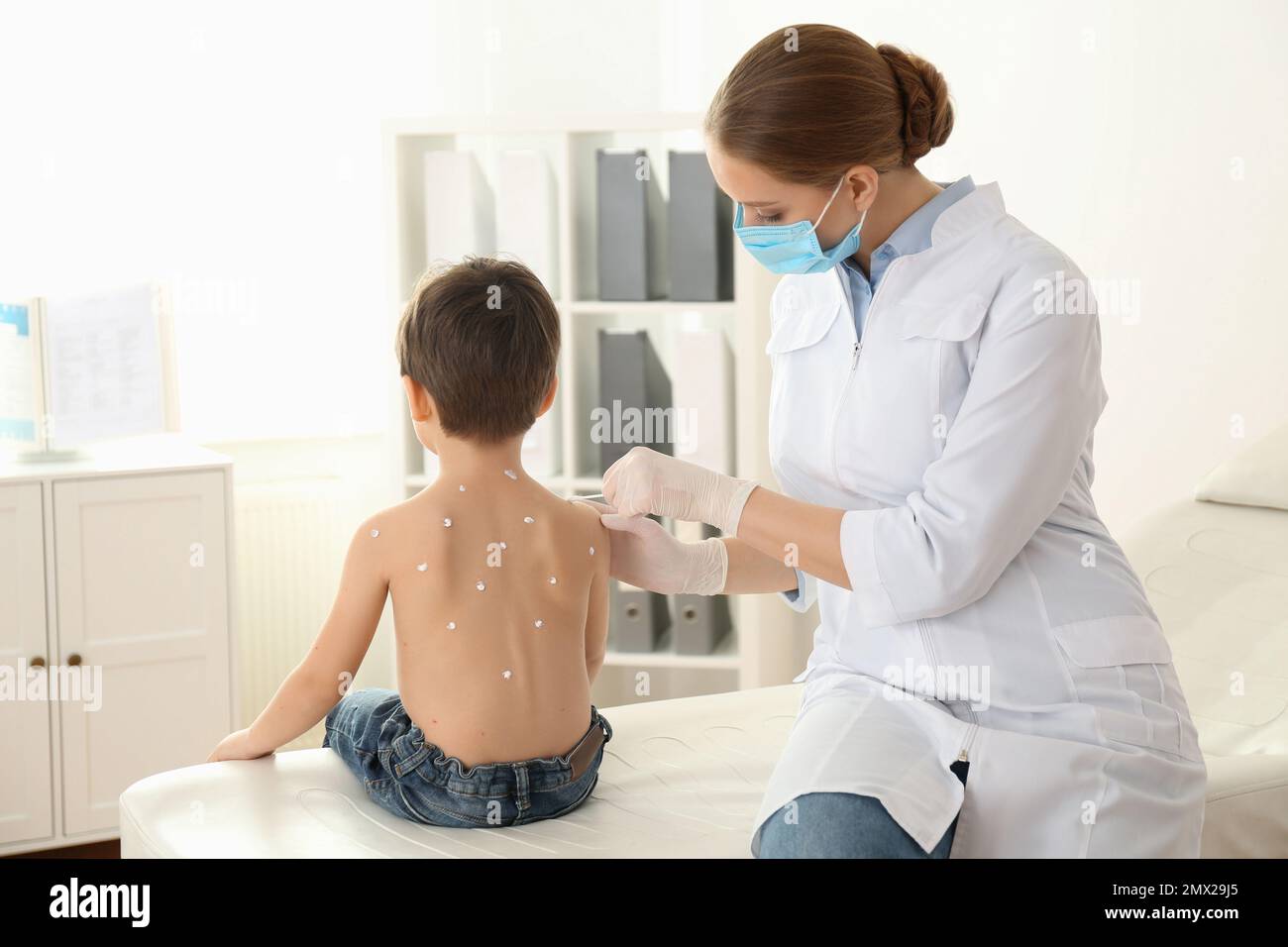 Chickenpox Doctor Doctor applying cream onto skin of little boy with chickenpox in clinic ...