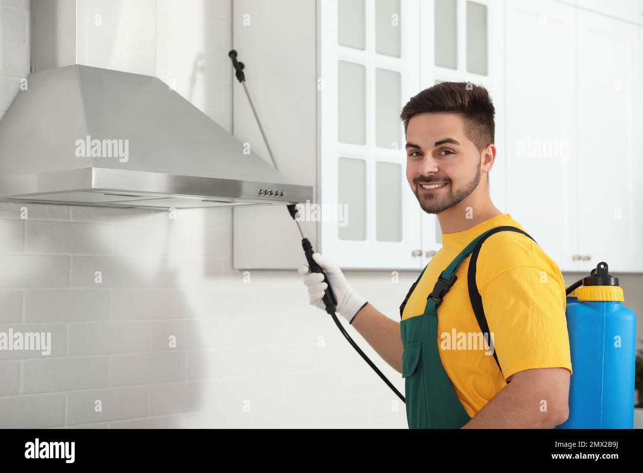 Pest control worker spraying insecticide on furniture in kitchen Stock