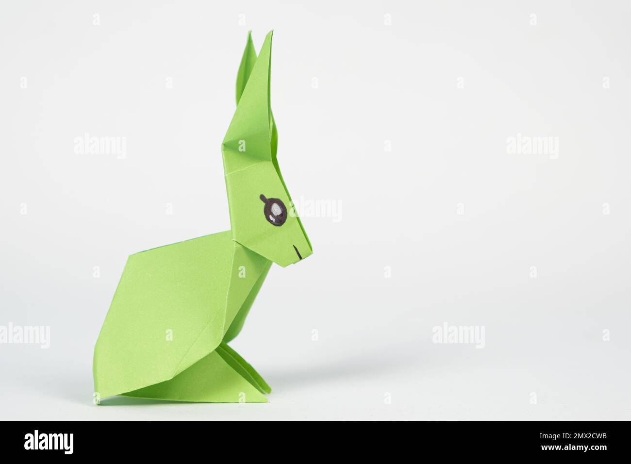 A green origami rabbit on a white background. Crafts for Easter, fold from paper, do it yourself, place for text. Stock Photo