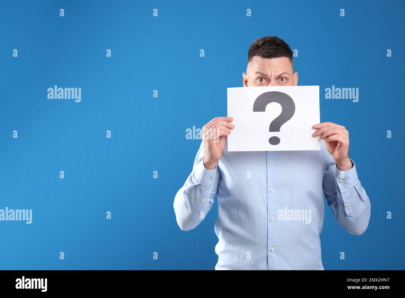 Emotional man holding paper with question mark on blue background. Space for text Stock Photo