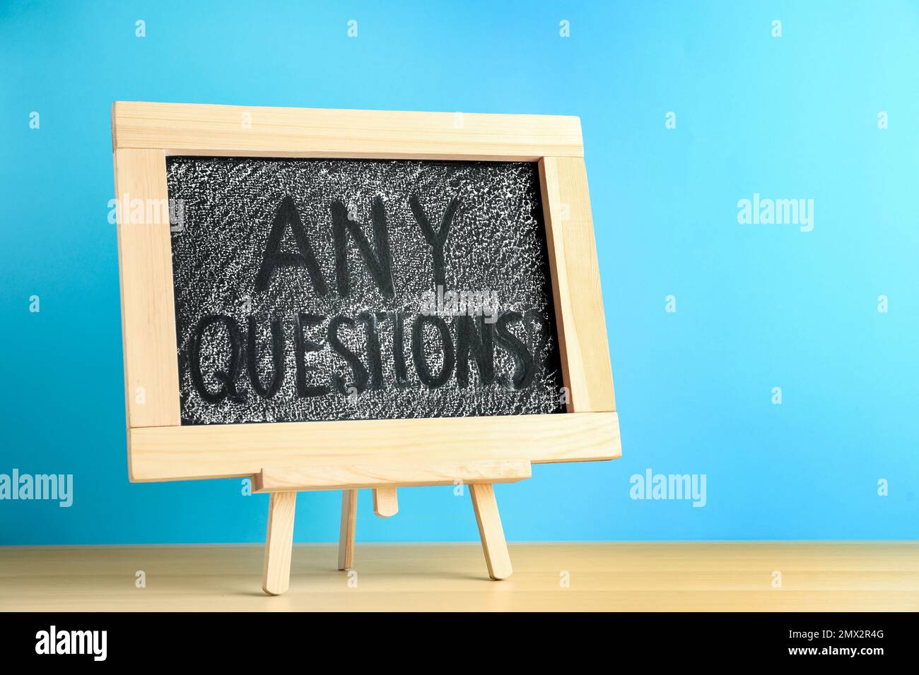 Blackboard with phrase ANY QUESTIONS on wooden table against blue