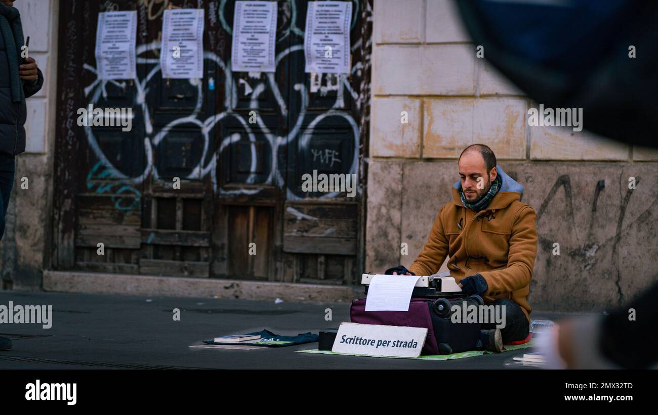 close-up of an artist on the street sitting on the ground writing his stories and poems as people pass him by Stock Photo