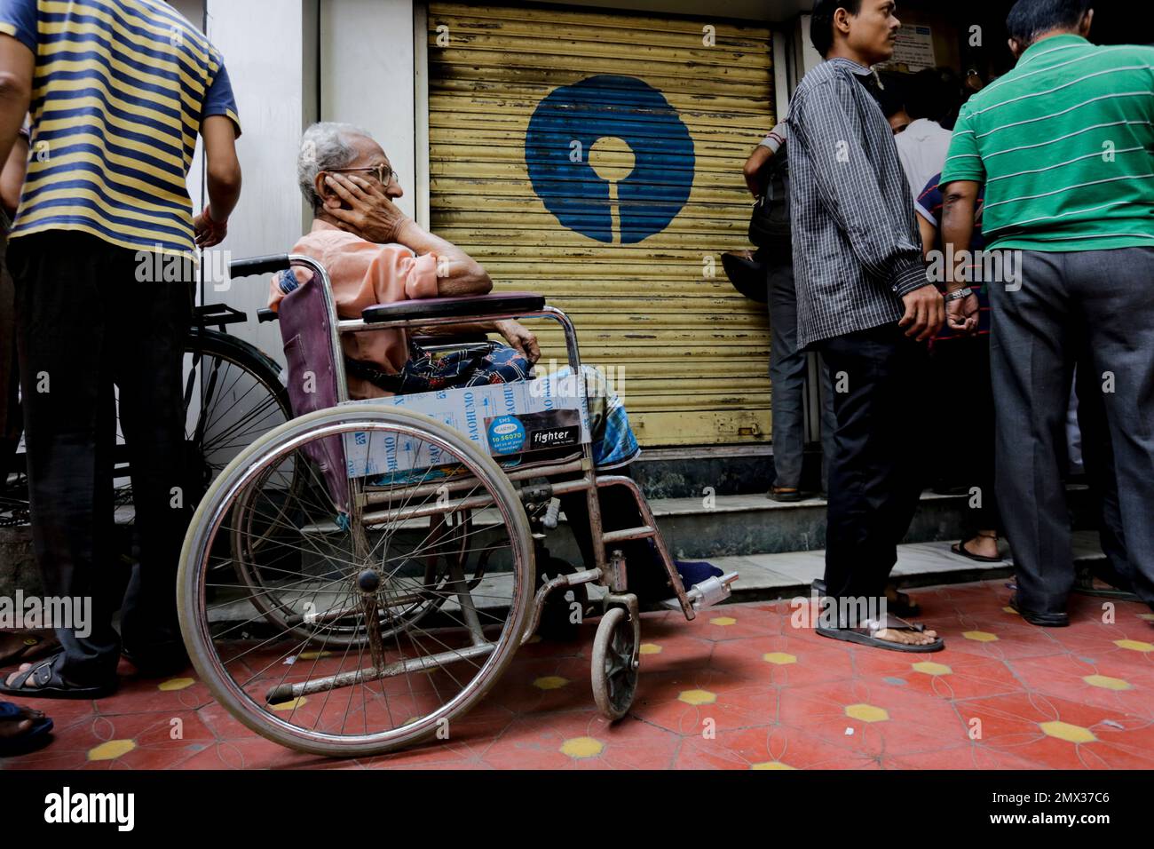 A physically disabled man on a wheel chair waits in queue to