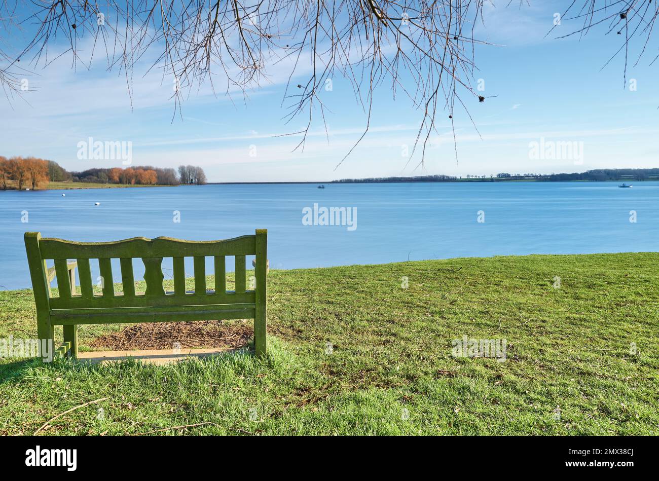 Peaceful, quiet, isolated bench at the shore of a lake on a sunny winter day. Stock Photo