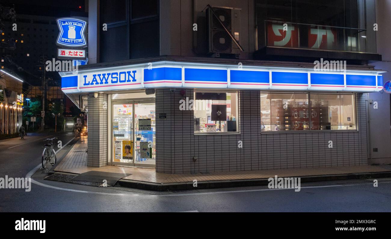 A night shot of the exterior picture of a LAWSON convenience store with its blue and white logo on a cloudy day with customers inside. Stock Photo