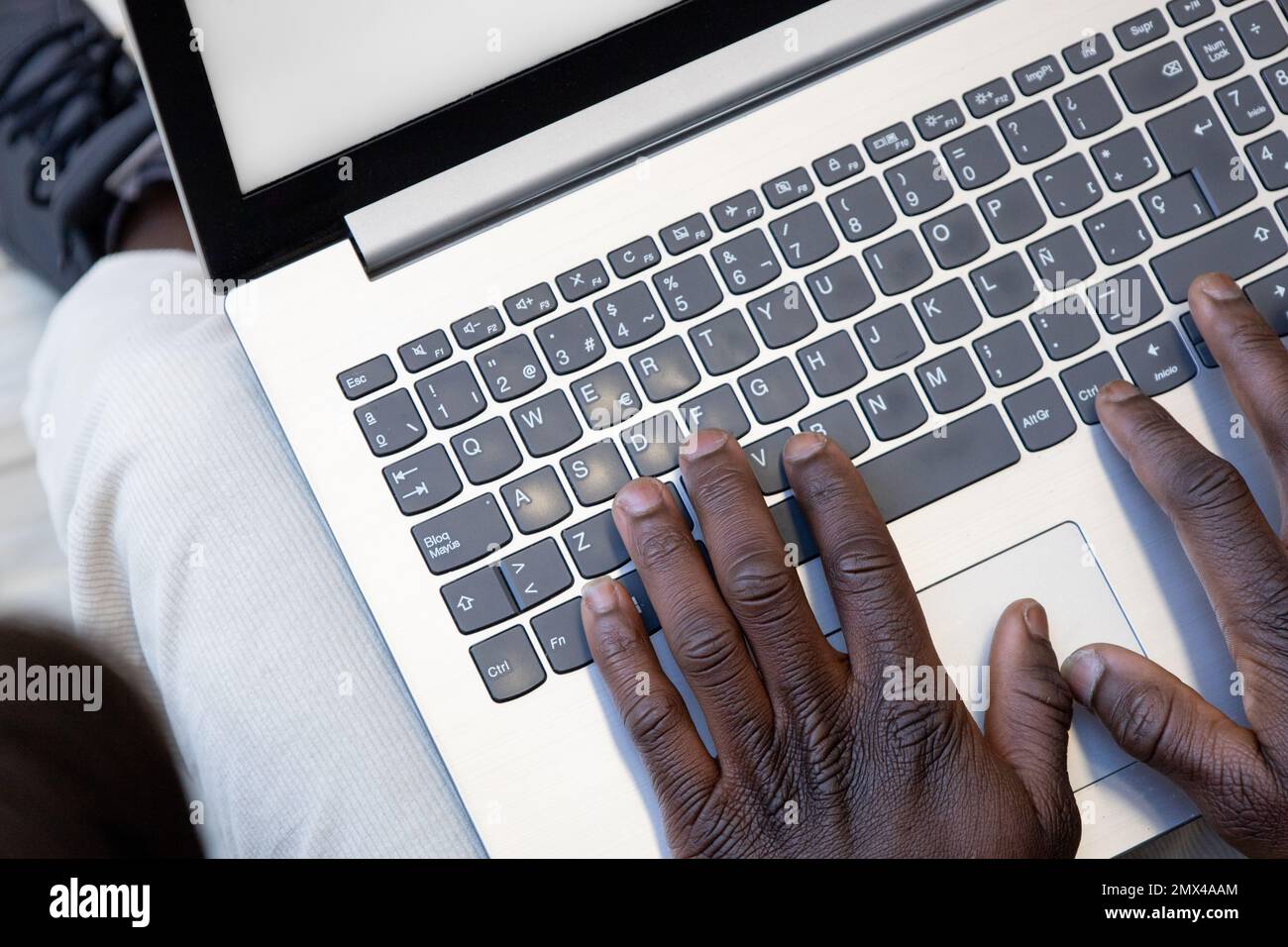 Close up african black hands typing on laptop computer keyboard on legs. Businessman response to email, online purchase. Work and social integration. Stock Photo