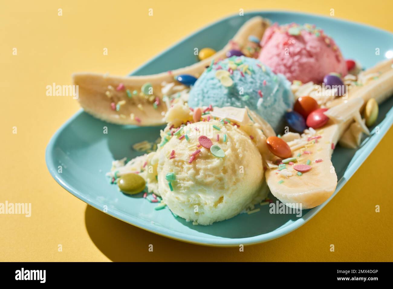 High angle of tasty banana slices served on plate with colorful balls of ice cream decorated with dragee and sprinkles on yellow table Stock Photo
