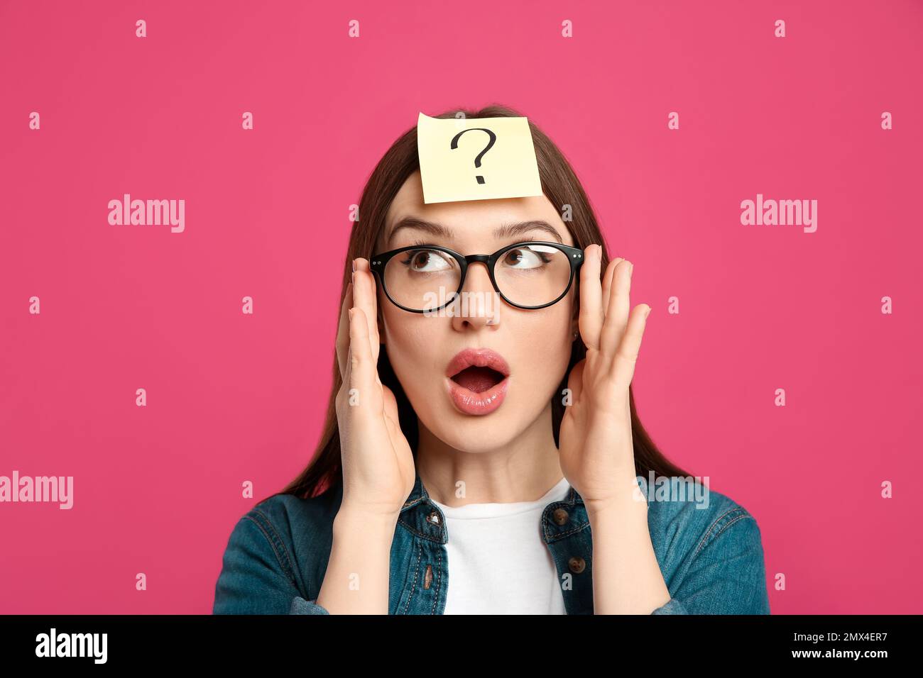 Emotional woman with question mark sticker on forehead against pink background Stock Photo