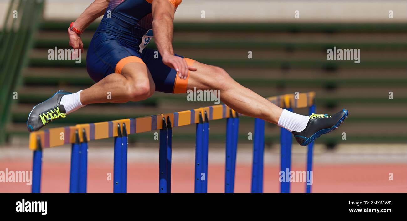 Athlete running a hurdle race in a stadium, runner jumping over an