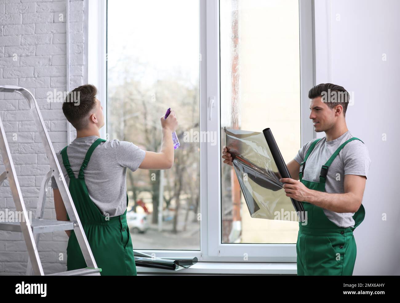 Professional workers tinting window with foil indoors Stock Photo