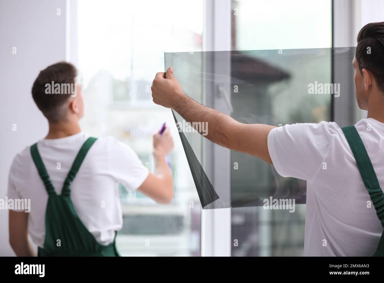 Professional workers tinting window with foil indoors Stock Photo