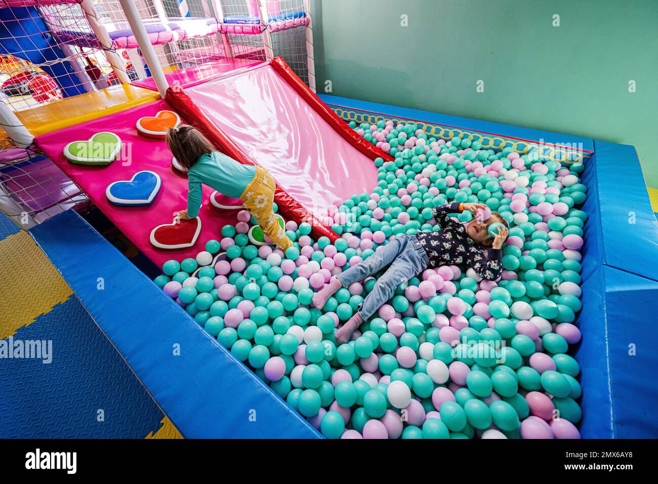 Happy sisters playing at indoor play center playground. Girl lying at