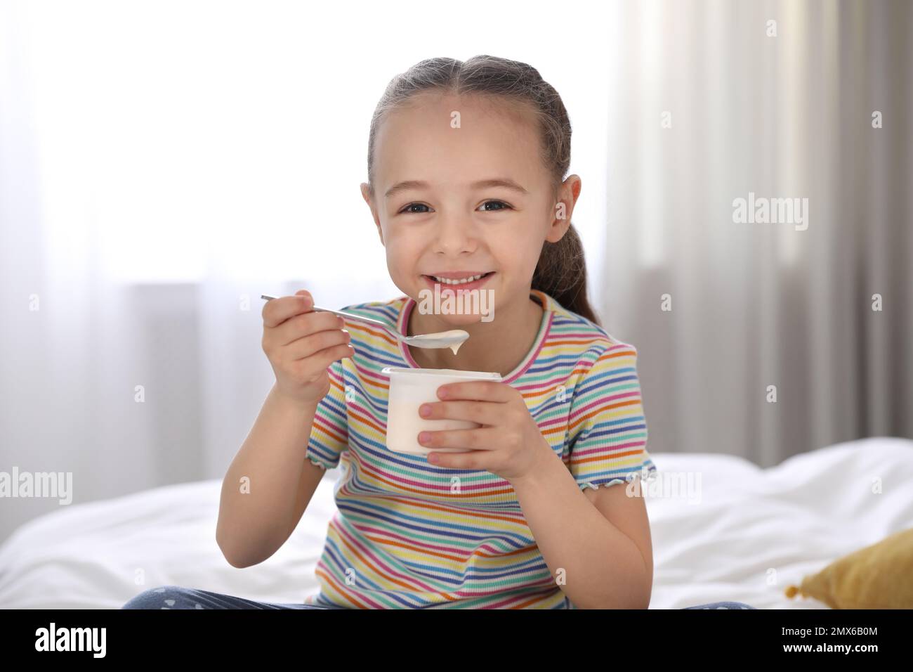 Cute little girl eating tasty yogurt on bed at home Stock Photo Alamy