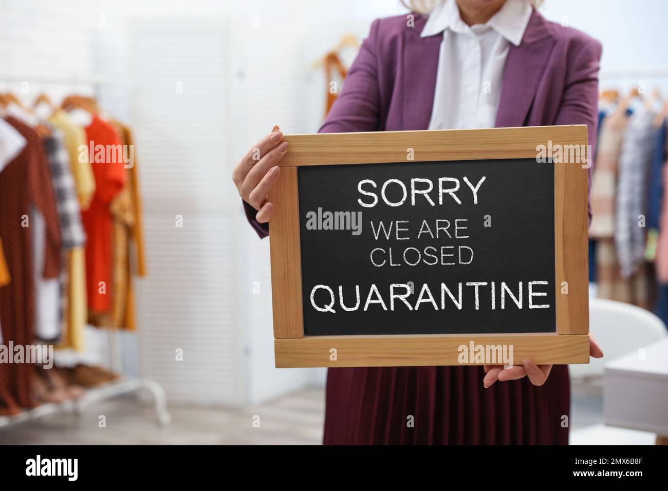 Business owner holding sign with text SORRY WE ARE CLOSED QUARANTINE in boutique, closeup Stock Photo