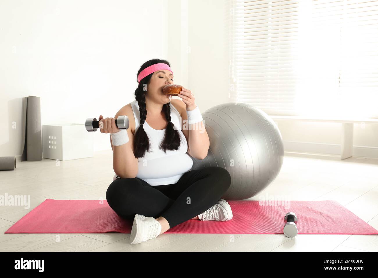 Lazy overweight woman eating bun at gym Stock Photo