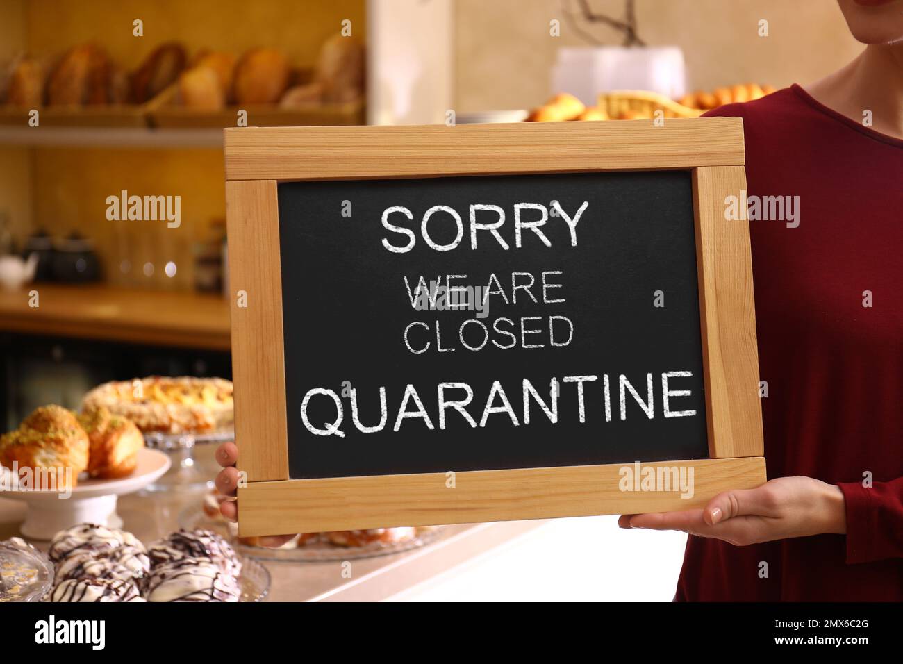 Business owner holding sign with text SORRY WE ARE CLOSED QUARANTINE in bakery, closeup Stock Photo