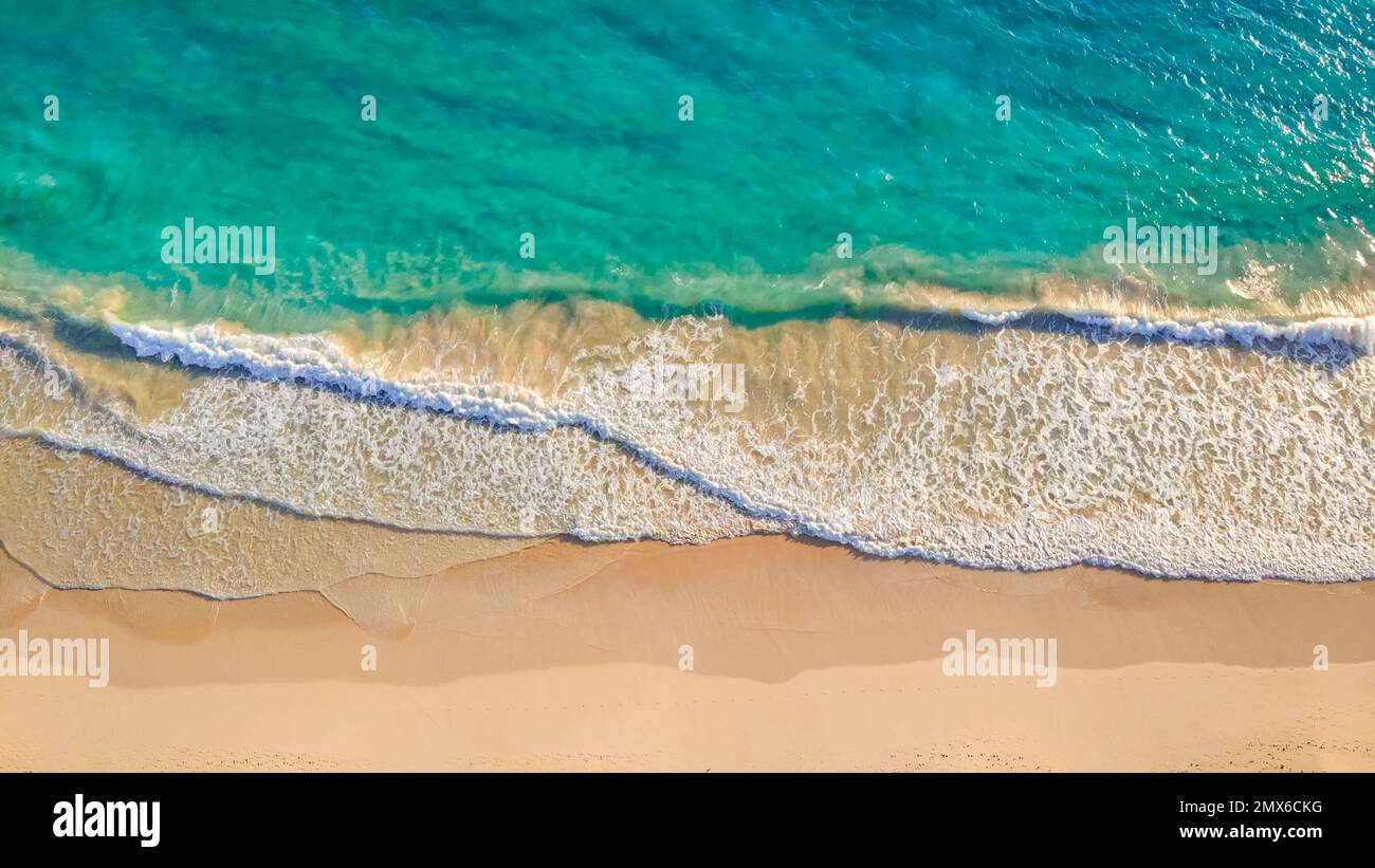 Close up of ocean waves rolling onto a beautiful beach with pink sand at sunrise. Sandy coastline with white turquiose sea waves. Soft wave of the sea on sandy beach with white clean foam Stock Photo