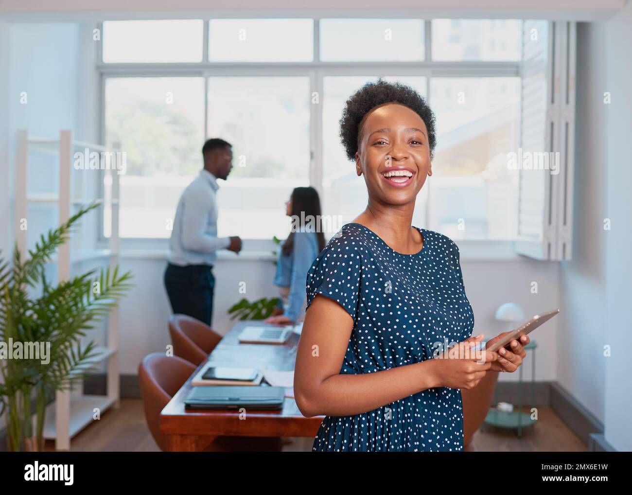 Young Black woman laughs in boardroom office using digital tablet Stock Photo