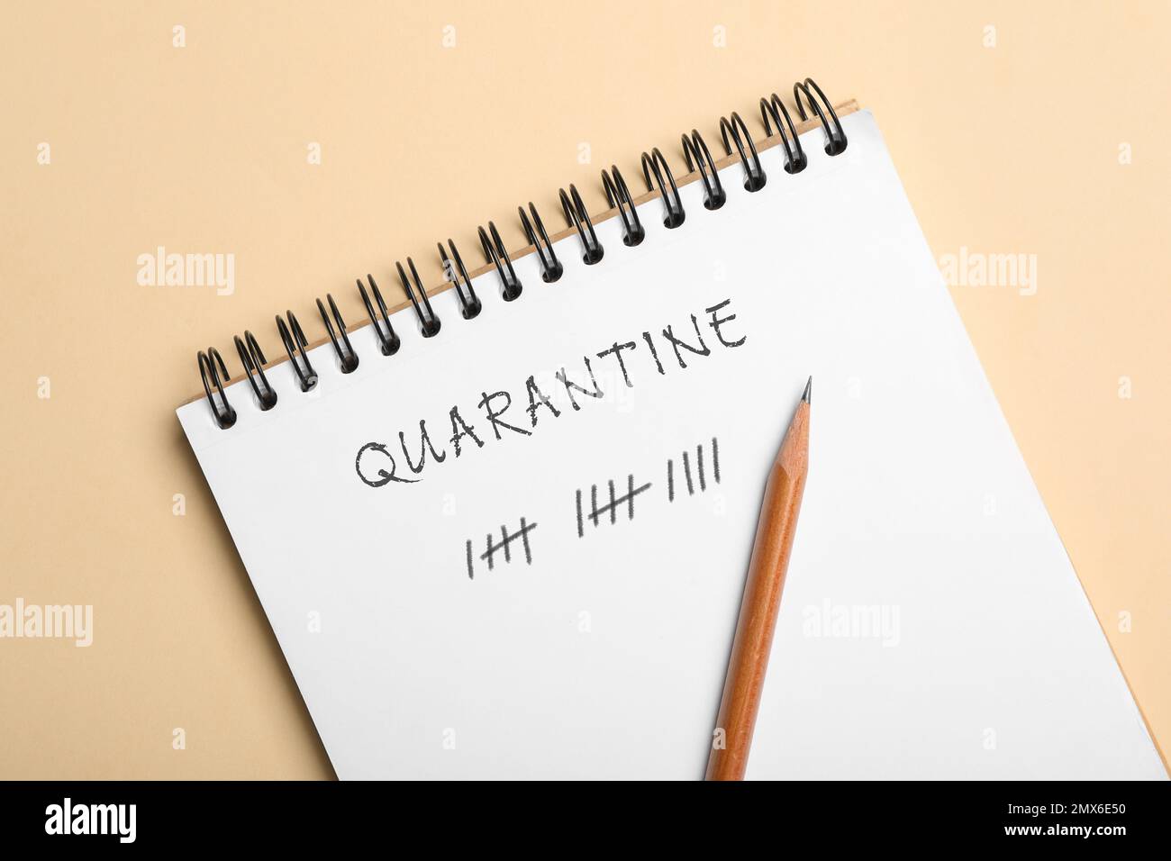 Open notebook and pencil on beige background, top view. Counting days of quarantine during coronavirus outbreak Stock Photo