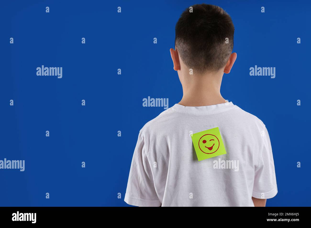 Preteen boy with winking face sticker on back against blue background, space for text. April fool's day Stock Photo