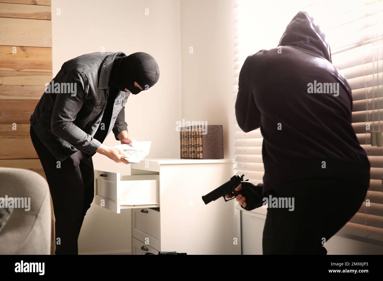Dangerous masked criminals with weapon stealing money from house Stock Photo