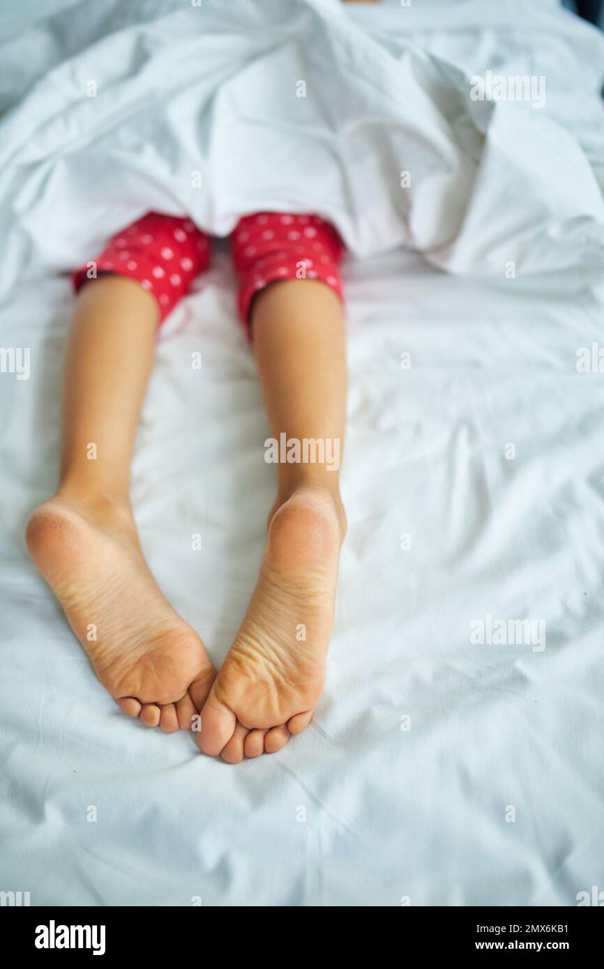 Girl's feet covered with white bed sheet, sleeping in a comfortable bed