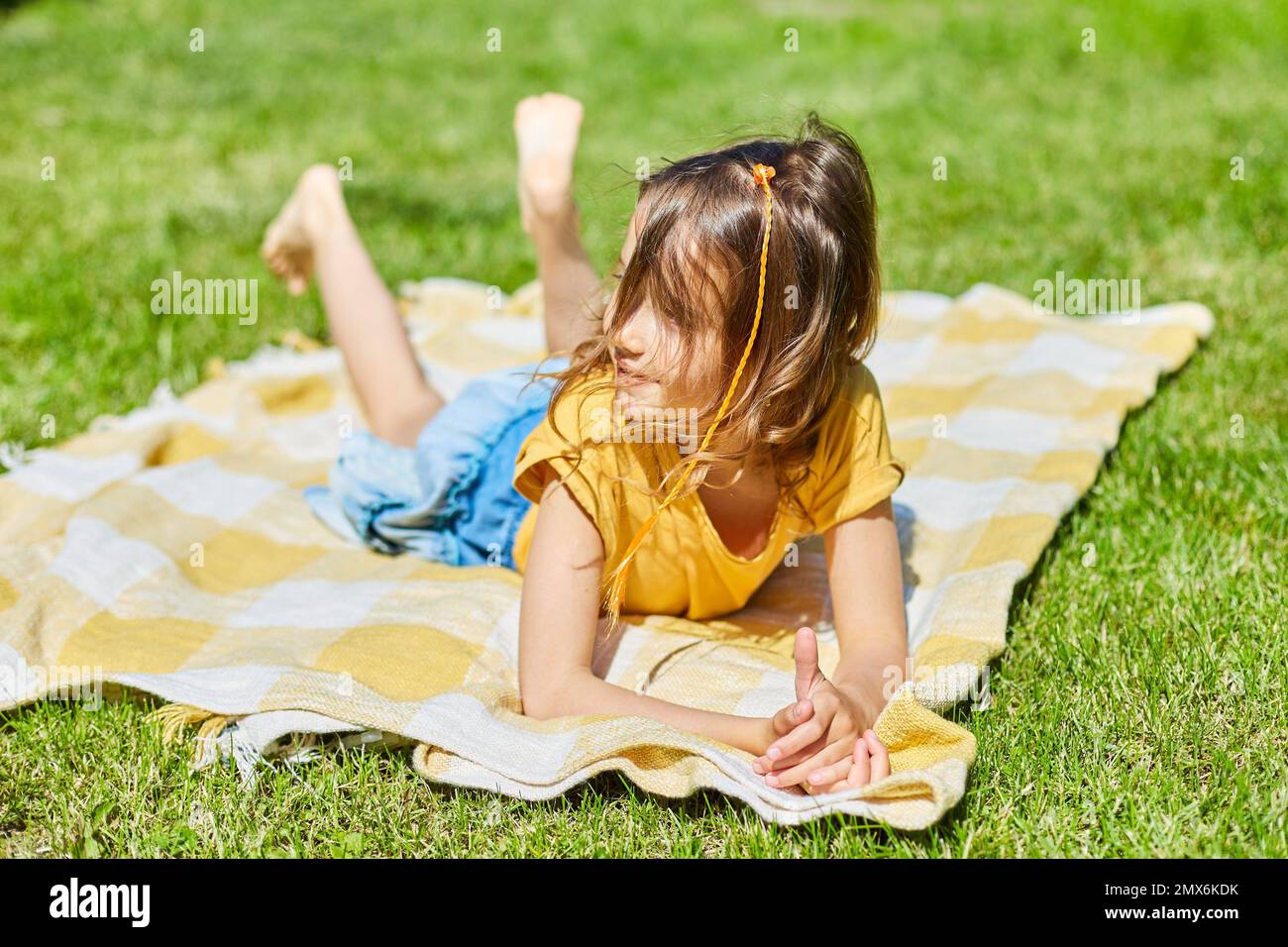 Child lying on the blanket, on the grass in the sun day, little girl take sunbathes on backyard of the house on a sunny summer day, summer time Stock Photo