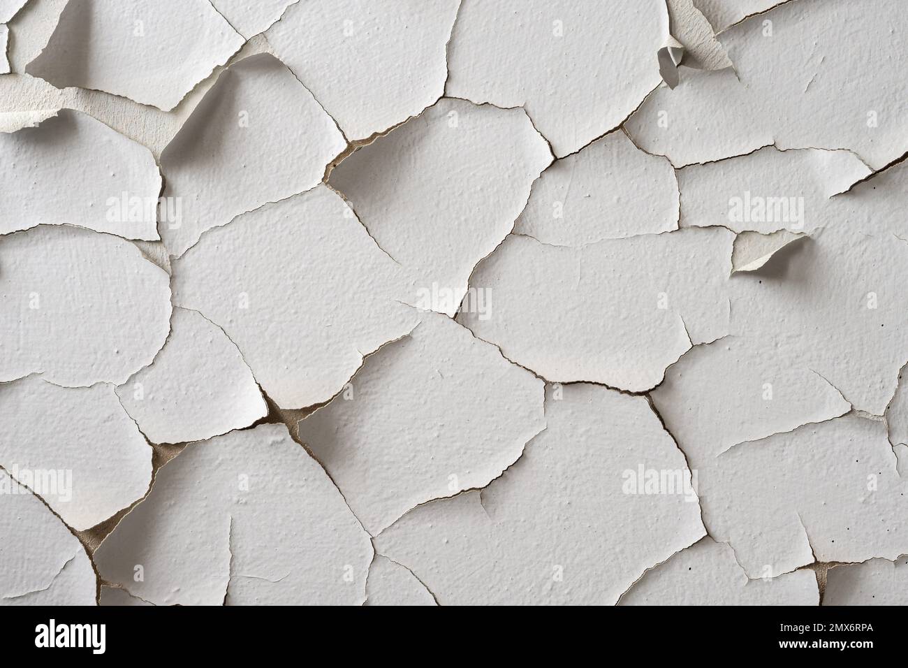 White painted wall with cracks and pieces of peeling paint. Flaky paint