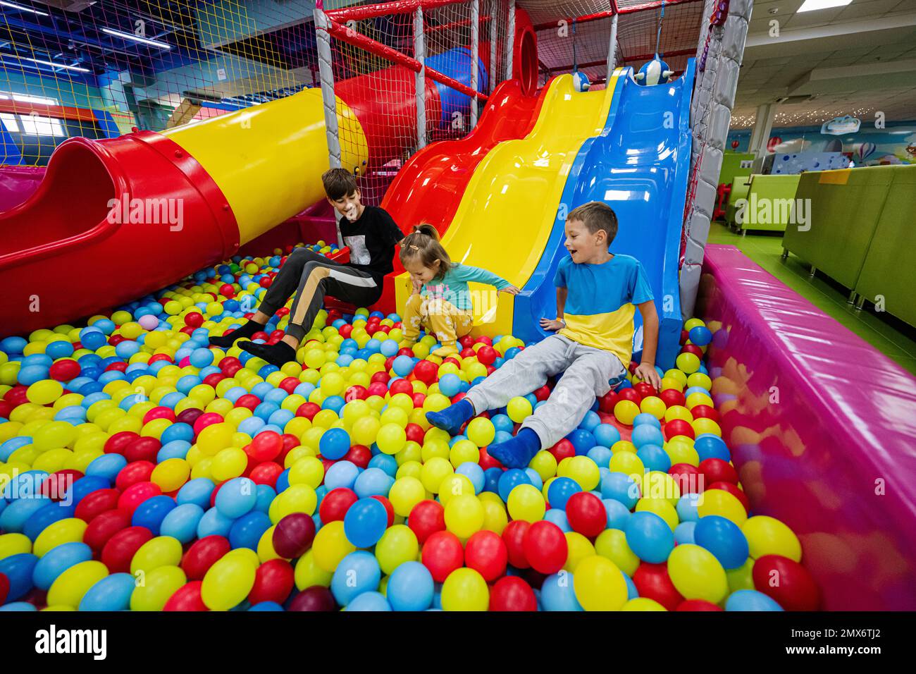 Happy kids playing at indoor play center playground. Children slides in colored slide into balls